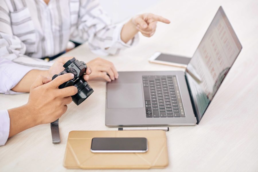 Crop shot of modern photographers with photo camera using laptop at table in office